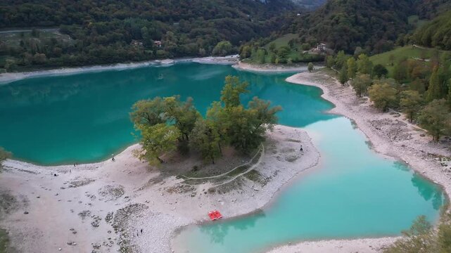 Aerial view of the turquoise waters of Lago di Tenno surrounded by lush green forests and rocky shores in Tenno, Trentino-Alto Adige, Italy.