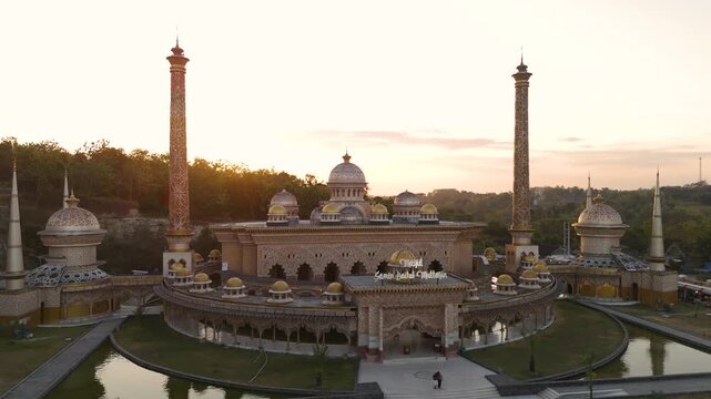 Aerial view of the ornate Masjid Samin Baitul Muttaqin mosque featuring tall minarets and golden domes at sunset in Bojonegoro, East Java, Indonesia.