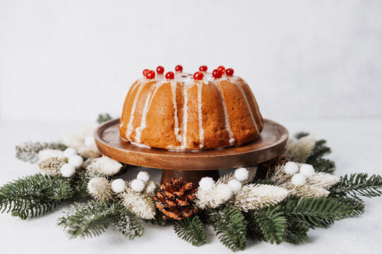 Homemade holiday bundt cake with sugar glaze and red cranberries on wooden stand surrounded by pine