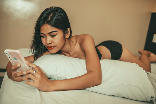 Adult woman in lingerie uses her smartphone in bed while exchanging flirtatious intimate messages with her boyfriend during a private conversation.
