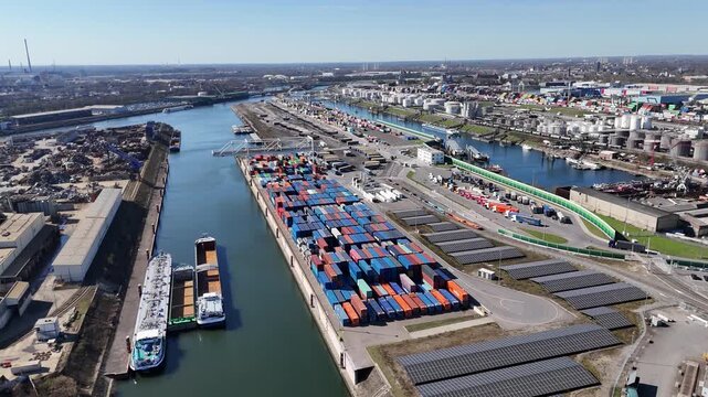 Smooth circular drone movement above stacked containers moored boats and the busy Duisport terminal area.