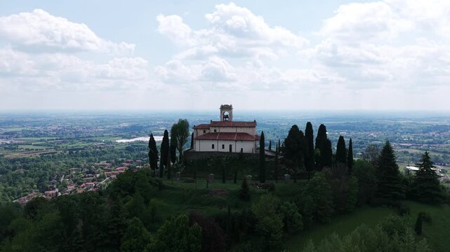 Sanctuary of Beata Vergine del Carmelo church on green hill overlooking valley in Montevecchia, Italy. Aerial drone orbiting, copy space