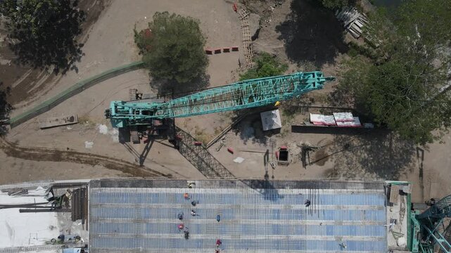 Aerial view of a large crawler crane and workers on a rebar-reinforced concrete structure at flyover girder construction site in Special Region of Yogyakarta, Indonesia.