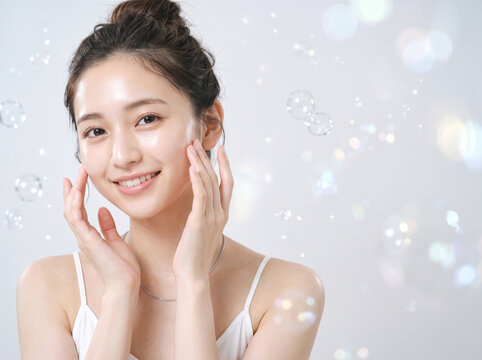 シャボン玉が舞う背景で両手を頬に添えて微笑む女性