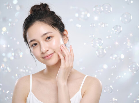 背景のシャボン玉と輝く光の中で頬に手を添えて微笑む女性