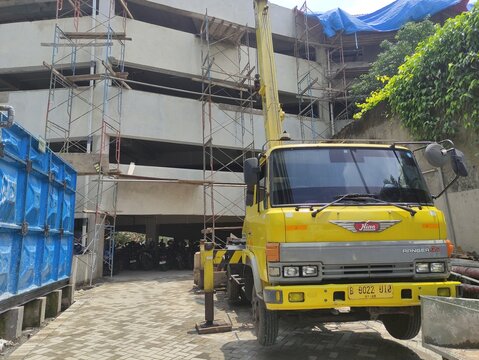 Bogor, Indonesia 31 Jan, 2025 - Urban construction site showing a building under development, scaffolding, construction materials, and a mobile crane truck under a bright sky, representing infrastruct