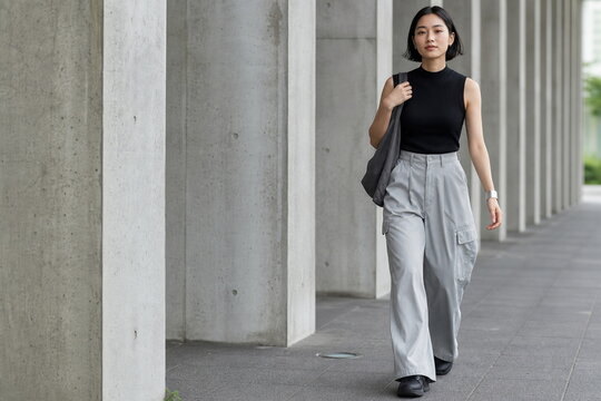 黒ニットと銀灰カーゴパンツでコンクリート柱列を歩く女性