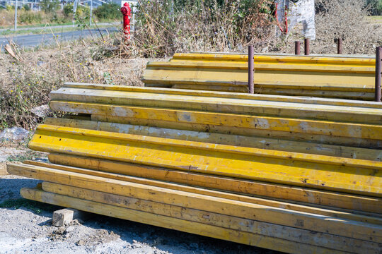 A stack of yellow wooden H20 formwork beams used for concrete shuttering sits outdoors at a construction site.
