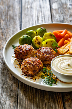 Fried pork meatballs with French fries, mini carrots and brussels sprouts on wooden table
