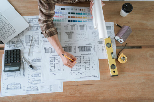 Architect working on house construction plans with blueprints, color samples, measuring tools and architectural drawings on a wooden desk.