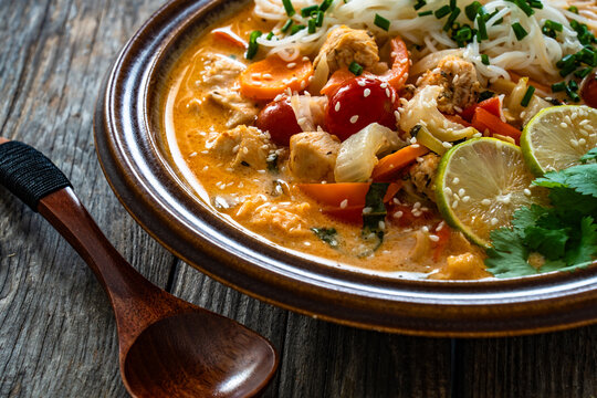 Tom Yum soup - Thai soup with chicken breast nuggets, vegetables and rice noodles on wooden table
