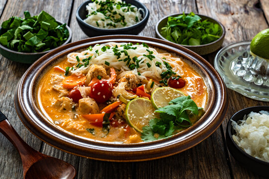 Tom Yum soup - Thai soup with chicken breast nuggets, vegetables and rice noodles on wooden table
