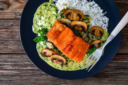 Fried salmon steak with creamy mushroom sauce and white rice on wooden table. Top view
