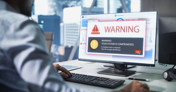 In Office Male Worker Uses a Desktop PC as Network Get Virus and Malware Infeceted, Display Showing Covers His Charts, System Hacked Skull Fills the Screen, Showing Ransomware