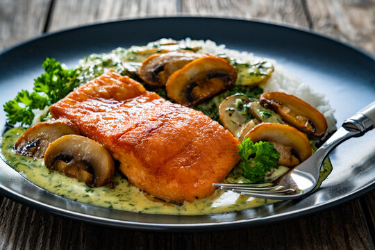 Fried salmon steak with creamy mushroom sauce and white rice on wooden table
