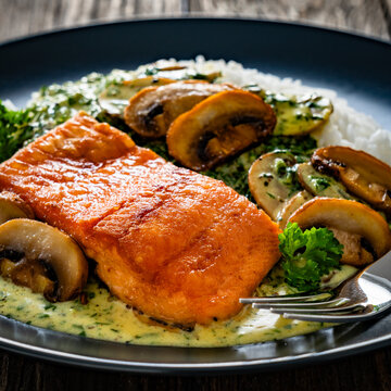 Fried salmon steak with creamy mushroom sauce and white rice on wooden table
