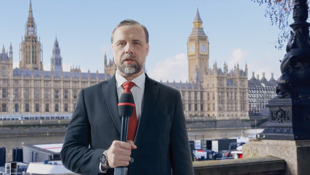  Reporter Speaks Into a Handheld Microphone While Presenting a Live News Update to Camera Beside the River Thames, the Houses of Parliament and Big Ben Filling the Backdrop