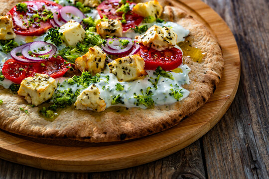 Vegetarian pizza with feta cheese, tomatoes, red onion and broccoli dip on wooden table
