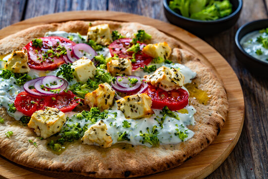 Vegetarian pizza with feta cheese, tomatoes, red onion and broccoli dip on wooden table
