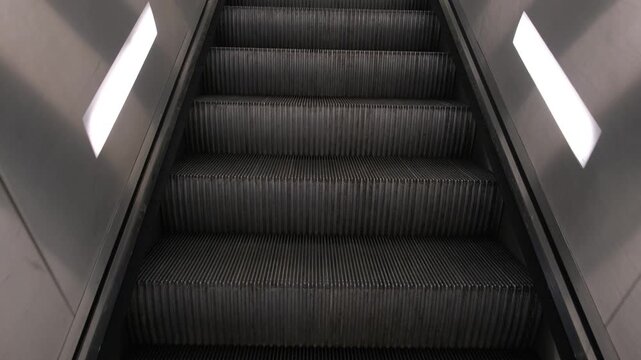 A low angle perspective view looking up empty moving escalator steps inside a clean modern transportation hub.