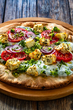 Vegetarian pizza with feta cheese, tomatoes, red onion and broccoli dip on wooden table
