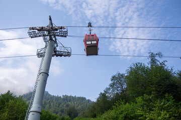 Red cable car gondola cabin moving on ropeway cable high above mountain forest trees. Real Photo © LariBat