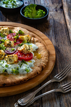 Vegetarian pizza with feta cheese, tomatoes, red onion and broccoli dip on wooden table

