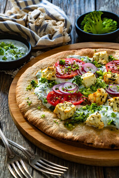 Vegetarian pizza with feta cheese, tomatoes, red onion and broccoli dip on wooden table
