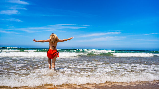 Beautiful middle-aged woman enjoying walk in ocean on sunny summer day. Back view
