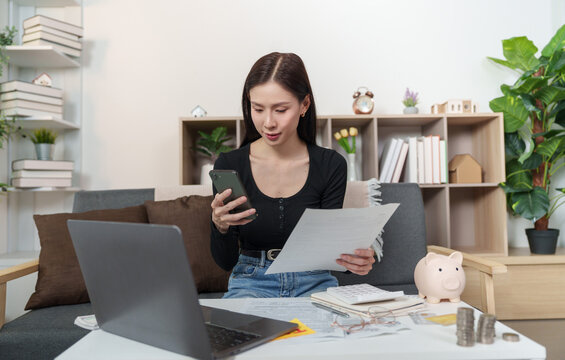Asian woman checking document and smartphone for online tax filing at home