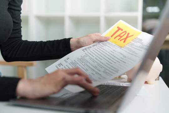 Cropped hands holding tax form with sticky note while using laptop for online tax filing