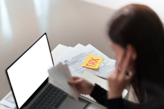 Woman reviewing tax forms and receipts at laptop for financial planning