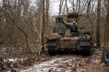 Obraz premium AHS Krab self-propelled howitzer of the Ukrainian Armed Forces camouflaged with a camouflage net and positioned in a winter forest. 