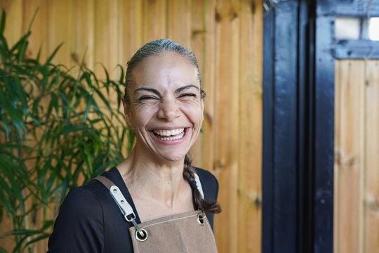Happy mature woman laughing in front of camera at coffee shop terrace - Waitress, job and lifestyle concept