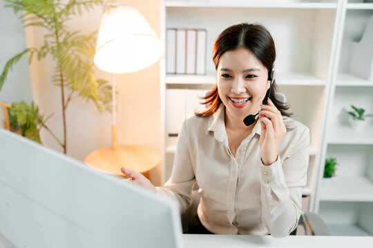 Young asian woman wearing a headset with a microphone. Actively engaging in a professional conversation while looking at a computer screen