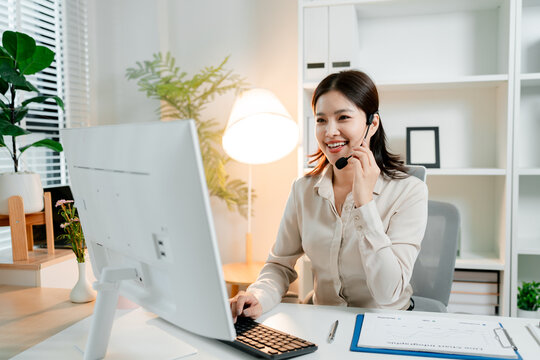 Young asian woman working remotely. Wearing a headset. Communicating virtually with customers on a computer