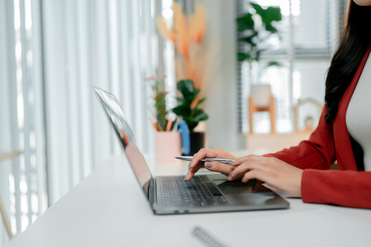 Young businesswoman typing on a laptop keyboard at her office desk, performing various tasks like data entry and online learning, showcasing a modern work environment