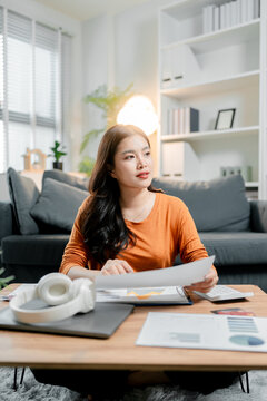 Young asian woman working from home, analyzing business documents and financial charts, managing finances and planning investments for future success, engaged in remote productivity