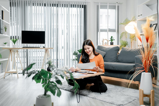 Young asian woman working from home, calculating finances and reviewing documents in a modern apartment, embracing flexible remote work and comfortable productivity
