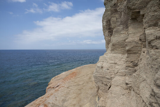 Steile Felsk&uuml;ste und markante Sandsteinformationen am Meer unter blauem Himmel mit leichten Wolken. Blick &uuml;ber das offene Wasser in einer K&uuml;stenlandschaft.
