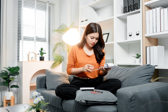 Young asian woman seriously managing personal finances. Sitting on a sofa at home. Reviewing receipts and calculating expenses with a calculator and credit cards