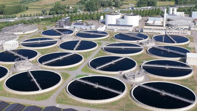 Aerial view of circular water treatment tanks at a wastewater facility with industrial infrastructure and surrounding green space in Den Hoorn, South Holland, Netherlands.