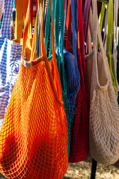Colorful reusable mesh and fabric tote bags hanging on a display rack