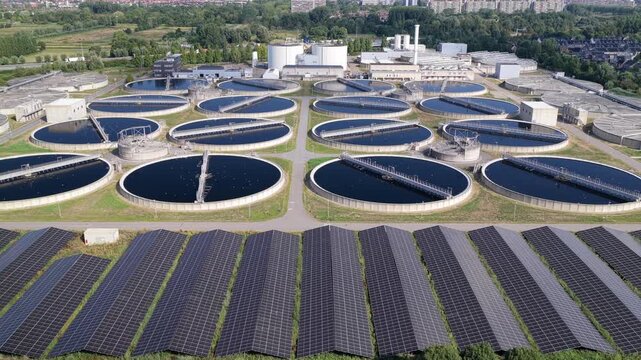 Aerial view of the water treatment plant featuring circular sedimentation tanks and large solar panel arrays in Den Hoorn, South Holland, Netherlands.