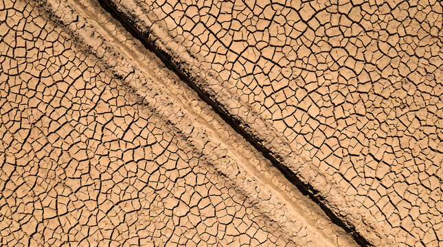 climate impact on agriculture. Cracked dry soil surface with visible tire tracks indicating drought conditions affecting agricultural land in a rural area