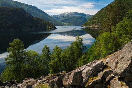 wide angle shot capturing the serene beauty of a deep blue Norwegian fjord framed by lush green forested ridges and distant mountain ranges in Sogn og Fjordane.