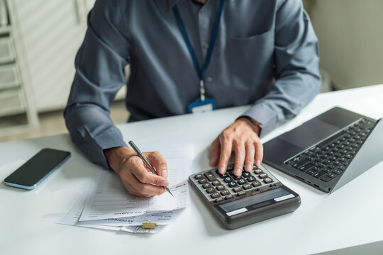 Close-up of office worker holding pen and using calculator to check financial bills and documents at desk.