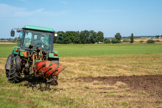 Farm tractor with moldboard plow turning soil in a harvested field
