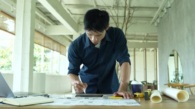Architect working on house construction plans with blueprints, color samples, measuring tools and architectural drawings on a wooden desk.