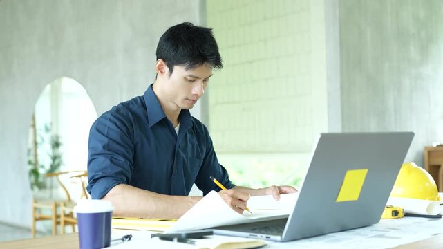 Architect working on house construction plans with blueprints, color samples, measuring tools and architectural drawings on a wooden desk.